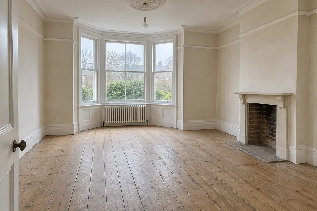 Sample empty living room before: bare floorboards, a bay window and an empty fireplace.