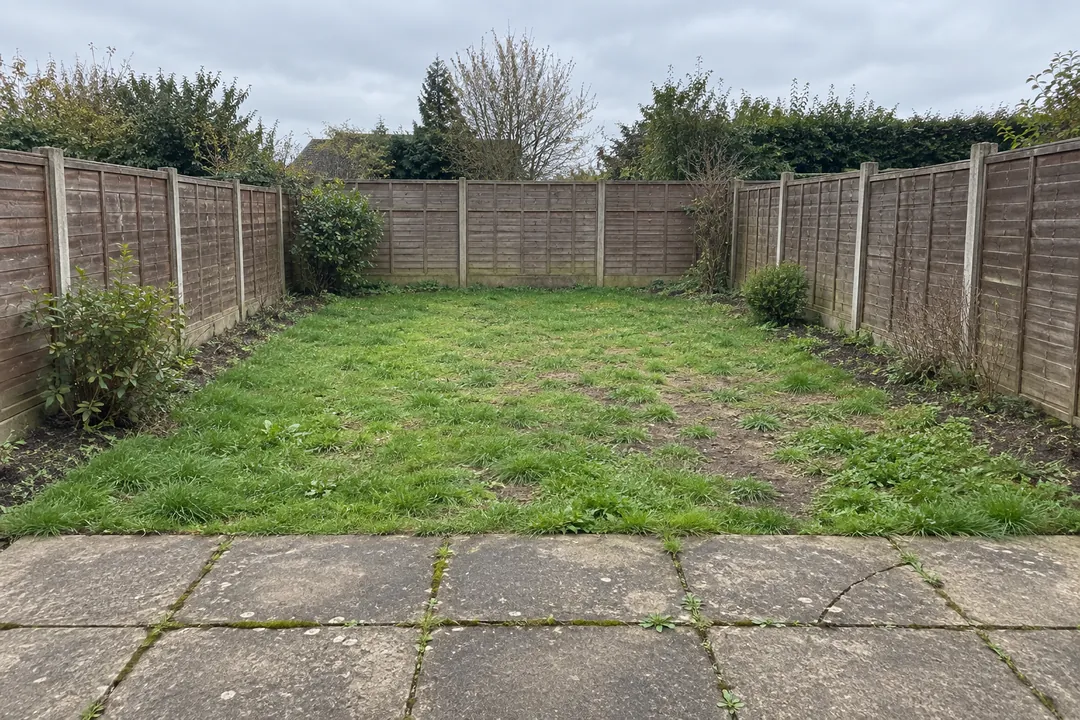 Sample backyard before: a patchy lawn between wooden fences and a cracked stone patio.